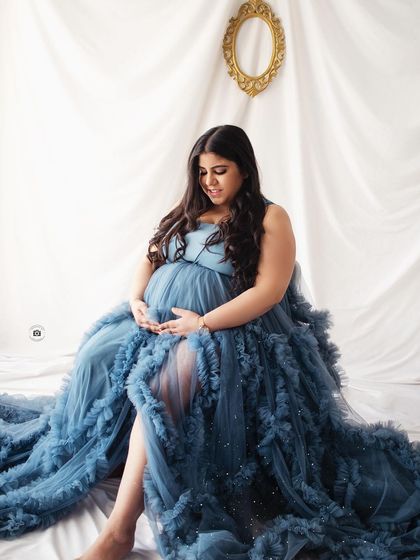 A peaceful moment captured as the mother-to-be sits, cradling her bump in a beautiful deep blue ruffled gown.