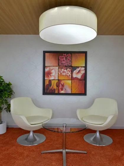 A quiet seating nook with two modern white chairs and a glass table. The space is defined by an orange carpet and floral artwork.
