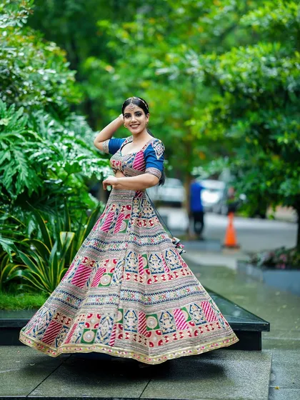 We love capturing the life and movement of a garment. Here, a model twirls in a vibrant, multi-colored ethnic lehenga, showcasing the full skirt and intricate patterns against a lush garden backdrop. This is a key shot for any Indian wear catalogue.