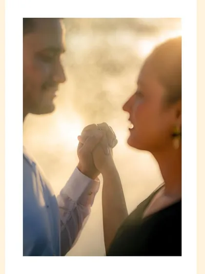 A close-up shot focusing on a couple holding hands, backlit by the golden hour sun, creating a hazy, dreamlike effect that emphasizes their connection.