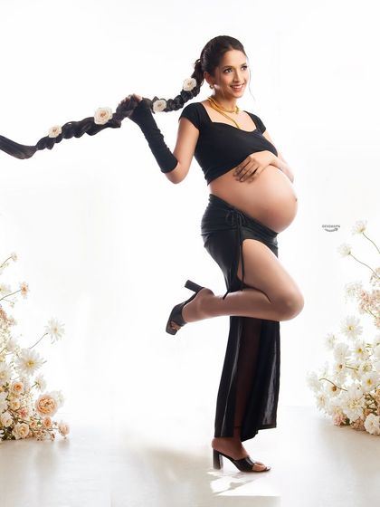 A playful and stylish portrait featuring a unique hairstyle and a modern black outfit. The floral setup adds a touch of softness and contrast to this fashion-forward maternity look.