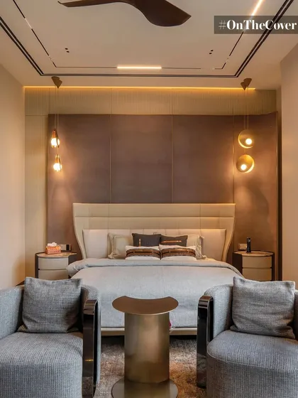 This master bedroom is a study in symmetry and calm. A textured headboard is flanked by elegant pendant lights, while two comfortable armchairs create a cozy seating nook, all within a warm, inviting color scheme.