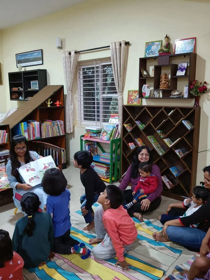 The children look up with anticipation as the storyteller reads from the book, wondering what will happen next to the paper dolls.