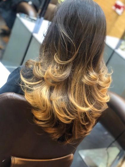 This is a classic ombre-balayage look, with a dark base transitioning into bright golden ends. The layered cut and soft curls help to blend the colors and create a voluminous, glamorous style.