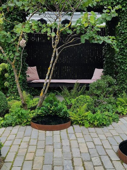This secluded seating area is built into the garden design. A long bench is framed by lush planting and a dark fence, creating a private and intimate corner for relaxation.