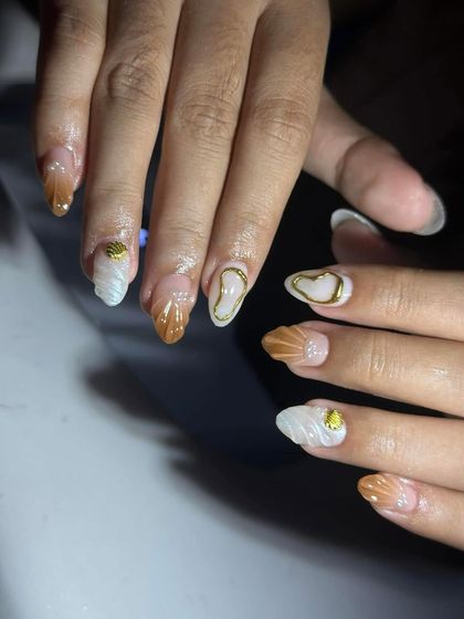 A close-up of seashell and chrome heart nail art. Notice the detailed texture on the white nail and the clean gold outline on the accent nail.