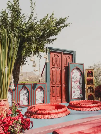 The 'Gulmohar Bagh' Haldi setup, featuring bold red decor elements and traditional seating against a stunning backdrop of the Udaipur hills.