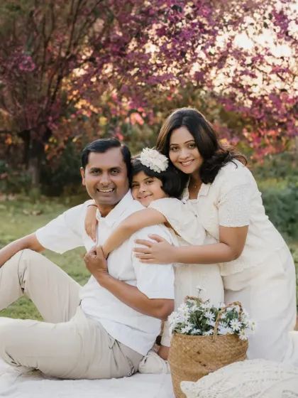 A family of three huddles together for a hug on a picnic blanket. The blooming pink trees in the background add a touch of spring magic to this outdoor portrait.