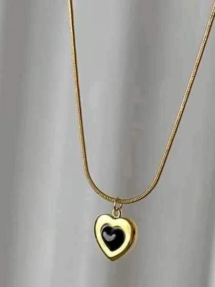 This unique necklace features a reversible heart pendant with a black enamel inlay on a sleek snake chain. It's a modern take on a classic design.