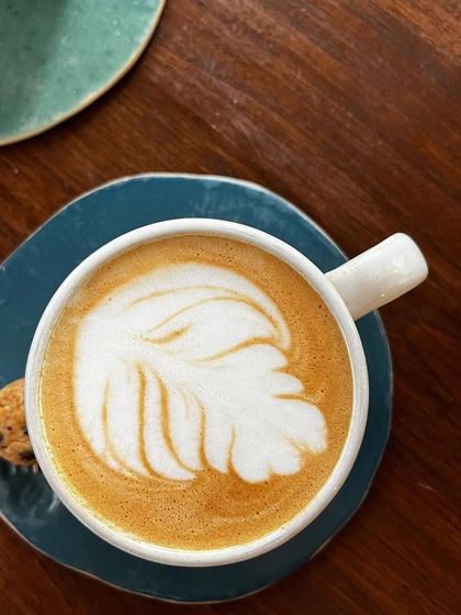 A perfect latte art shot. The focus is entirely on the beautifully executed leaf pattern in the foam, showcasing the skill of the barista and the quality of the coffee. It's a classic and essential shot for any coffee shop.