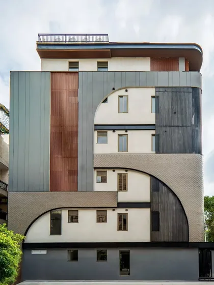 A straight-on shot of the Patel Nagar facade, highlighting the clean geometry and dramatic curves. The composition of different claddings and textures creates a visually interesting and minimal architectural statement.