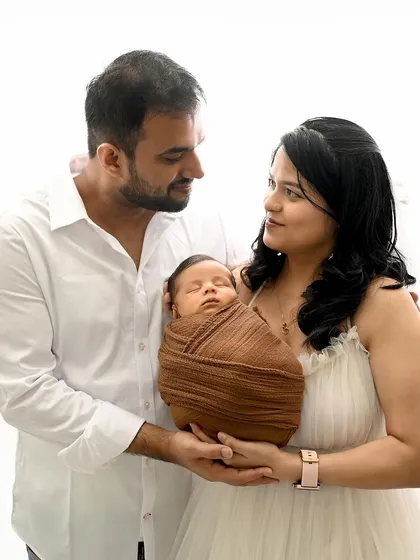 A classic family pose with a newborn. The parents hold their baby together, creating a beautiful portrait that focuses on their new family unit in a simple, white studio setting.