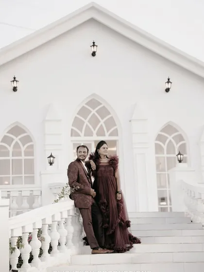 A stylish couple poses on the grand white staircase of a church-like studio set, showcasing a sophisticated and elegant pre-wedding photography theme.