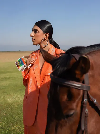 This shot captures a candid, windswept moment between a model and a horse, highlighting fashion accessories. The open space and natural elements add a sense of freedom and movement.