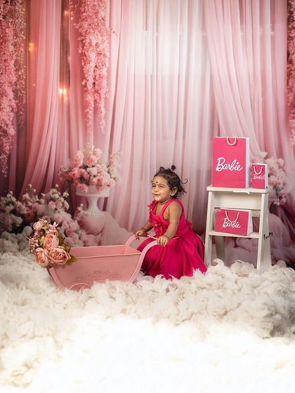 A candid moment in a Barbie world. This little girl enjoys her magical pink setup, complete with a floral cart and fluffy clouds.