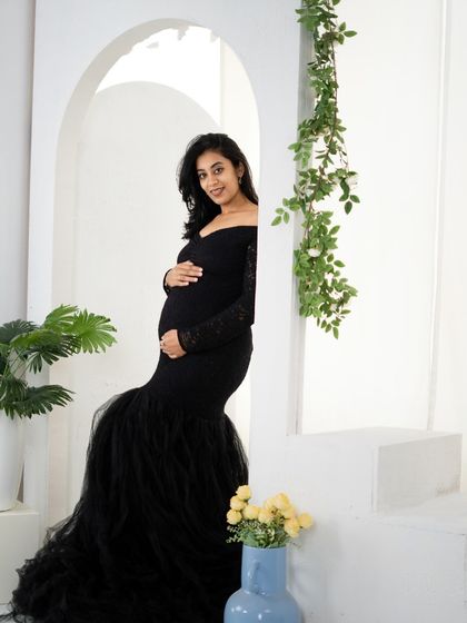 A classic black mermaid gown with lace sleeves, photographed in our minimalist white archway setup. The contrast between the dark dress and the bright background creates a timeless and elegant look.