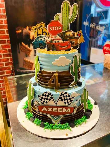 A two-tier cake inspired by the movie 'Cars', with Lightning McQueen and Mater in a desert scene.