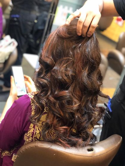 The client is checking her phone, but her hair is the star. The mix of highlights and curls creates a full, luxurious look that is perfect for any occasion.