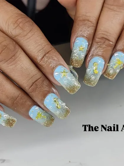An under-the-sea themed manicure with a blue and gold glitter base, adorned with 3D starfish, seahorses, and pearl "bubbles".