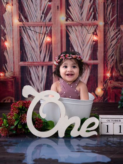 A rustic first birthday setup. The combination of the wooden backdrop, warm lights, and a happy baby in a tub creates a cozy and charming scene.
