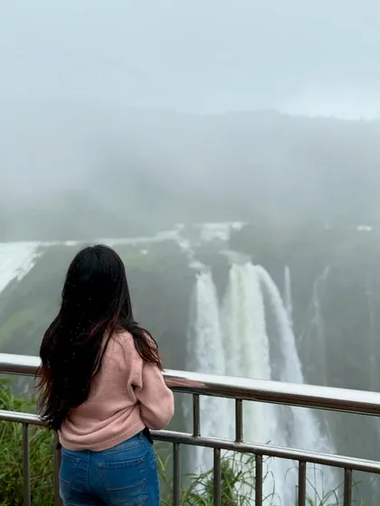 A lone trekker gazes at the powerful cascade of Jog Falls, a moment of quiet contemplation.