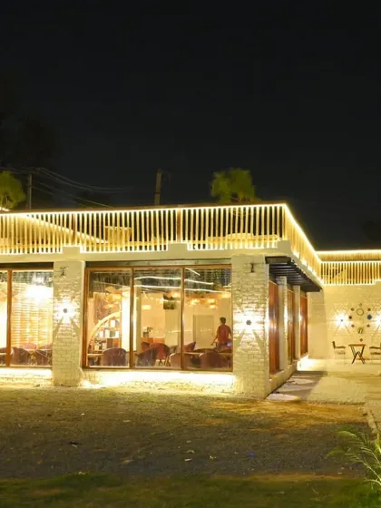 A wide shot of the cafe's exterior at night. The architectural lighting highlights the modern design and makes the building stand out.