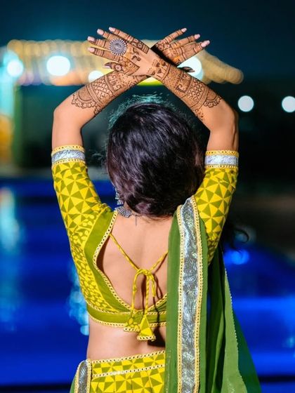 A beautiful shot of a bride posing against a pool backdrop. Her back-hand mehndi design looks stunning and adds to the artistic feel of the photo.