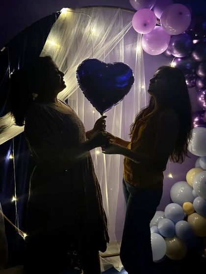 A sweet moment between two friends holding a heart-shaped balloon. The silhouette effect against the lit backdrop creates a very memorable photo.