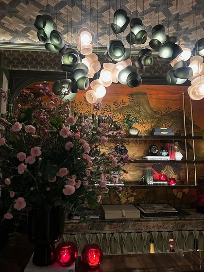 An installation of the Bocci 100 series at India Design 2025, mixing dark and light pink pendants. The fixture is set against an ornate backdrop, creating a rich, layered look.