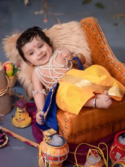 A happy baby Krishna lounging on a miniature sofa, surrounded by colorful props. This overhead shot captures a moment of pure, relaxed joy during the session.
