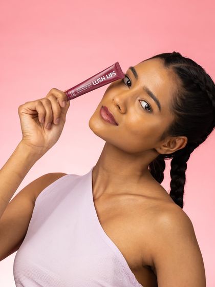 This pose is confident and direct. The model holds the product near her eye, drawing attention to both her face and the lip gloss tube in a way that feels modern and engaging for social media.