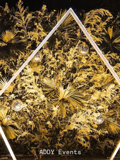 A unique photo backdrop featuring a geometric frame, dried golden palm leaves, and sparkling disco balls.