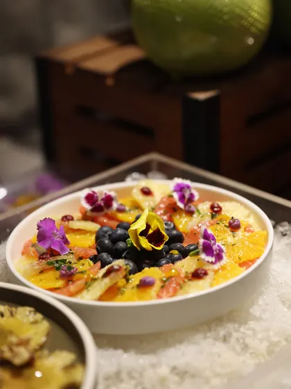 A refreshing fruit salad with citrus segments, blueberries, and pomegranate, adorned with edible flowers for a touch of natural beauty.