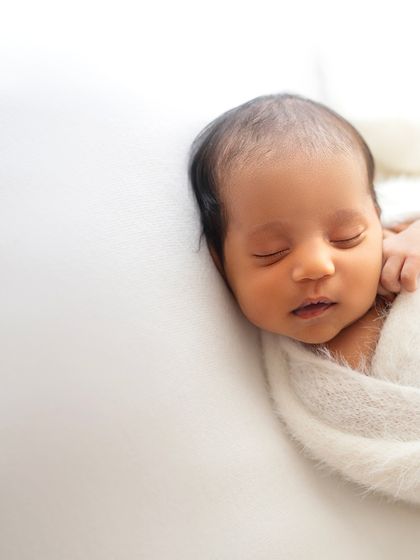 A classic and simple portrait of a newborn wrapped in a soft, fuzzy white blanket. The focus is entirely on their peaceful, sleeping face.