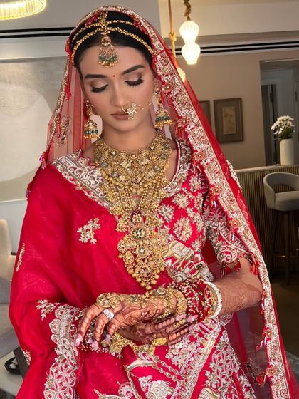 A serene portrait of a traditional bride. Her hair is styled in a sleek bun with a center part, perfect for her elaborate matha patti.