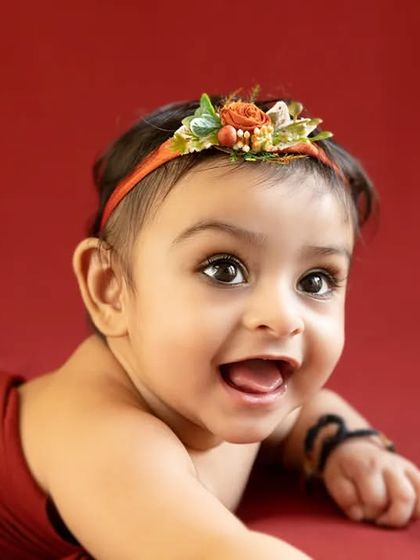 A happy baby girl enjoys tummy time on a red backdrop during her milestone session.
