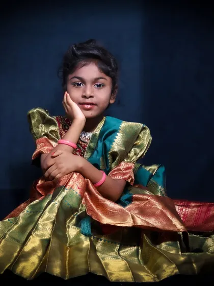 A classic studio portrait of a young girl in a stunning traditional pattu pavadai. I use simple, elegant lighting to focus on her confident pose and the beautiful details of her outfit.