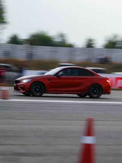 Another shot of the red BMW M2 at speed, showcasing its classic coupe proportions and track-ready stance.