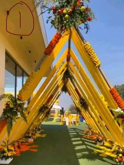 I build impressive entrances like this triangular walkway tunnel. It is constructed with bamboo, wrapped in bright yellow fabric, and decorated with fresh marigold flowers for a Haldi or Mehendi ceremony.