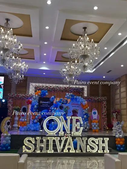 For this first birthday, we went to outer space. This wide shot shows the complete stage decoration in a banquet hall, featuring large marquee letters for the child's name and age, a custom space-themed backdrop, and extensive balloon work to create an immersive experience.