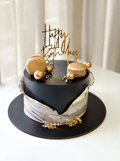 A sophisticated black birthday cake with a marble-patterned wrap and gold accents. I added golden macarons and a modern "Happy Birthday" topper to complete the elegant look.