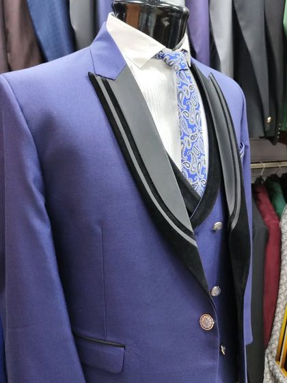 A royal blue three-piece suit designed for a groom or for party wear. The black velvet detailing on the lapels adds a touch of luxury and contrast, making it a standout choice.