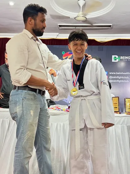 A happy moment as our Taekwondo fighter receives his gold medal from the coach.