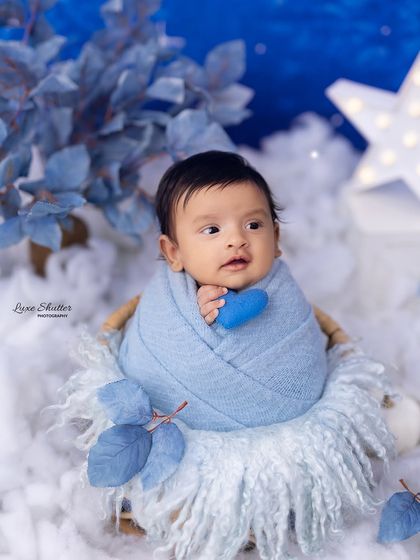 A peaceful newborn boy swaddled in blue, nestled in a soft, cloud-like basket against a dreamy, starry night backdrop. This celestial theme is a popular choice for baby boy photoshoots.