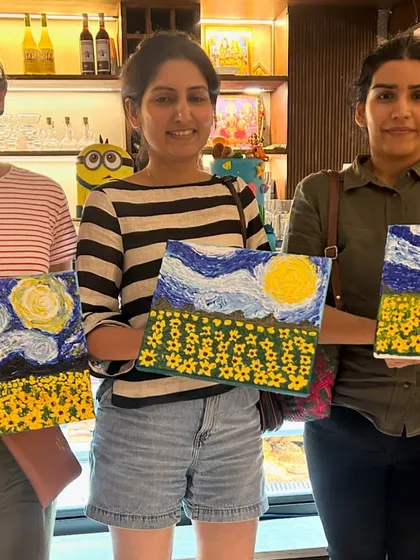 A trio of friends proudly displaying their textured sunflower and sky paintings. These workshops are a perfect creative hangout.