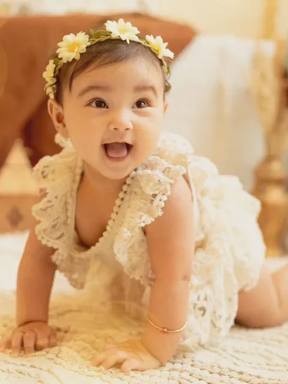 A perfect sitter session portrait. This baby girl, dressed in a lovely lace romper, shows off her crawling skills with a big, happy smile.