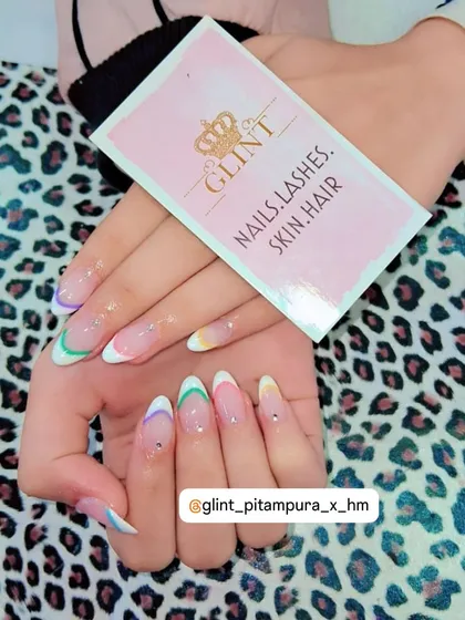 A modern take on the classic French manicure. This design features a clear base on almond-shaped extensions with delicate, multi-color pastel tips and a single rhinestone accent, showcasing a trendy and playful nail art style.