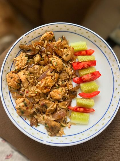 A one-bowl meal of chicken and mushroom rice, served with a side of fresh cucumber and tomato salad.