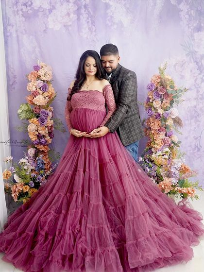A loving family portrait. The couple embraces while the mom-to-be cradles her bump, all framed by beautiful pastel floral arrangements.