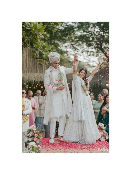 The celebration of a lifetime begins. This shot captures the couple's triumphant moment post-Varmala, hands raised in joy amidst a rain of petals from their loved ones.